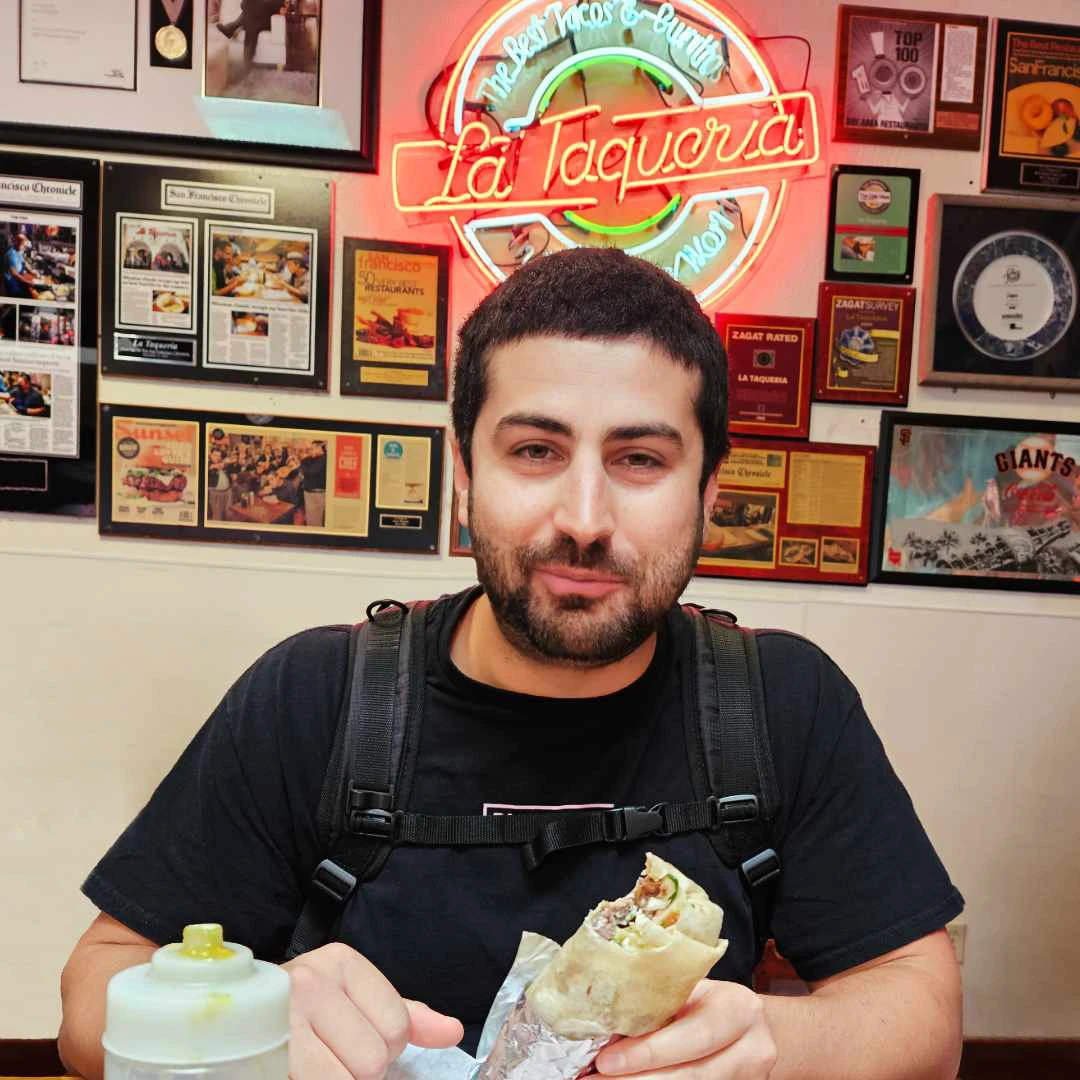 Tim eating a burrito and smiling in front of the restaurants neon sign.