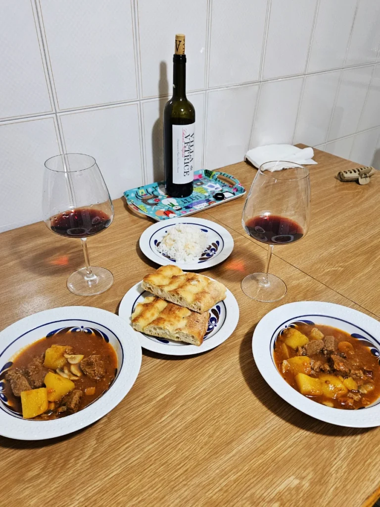 Two bowls of beautifully prepared Italian beef stew accompanied by two pieces of sliced focaccia and two glasses of wine.