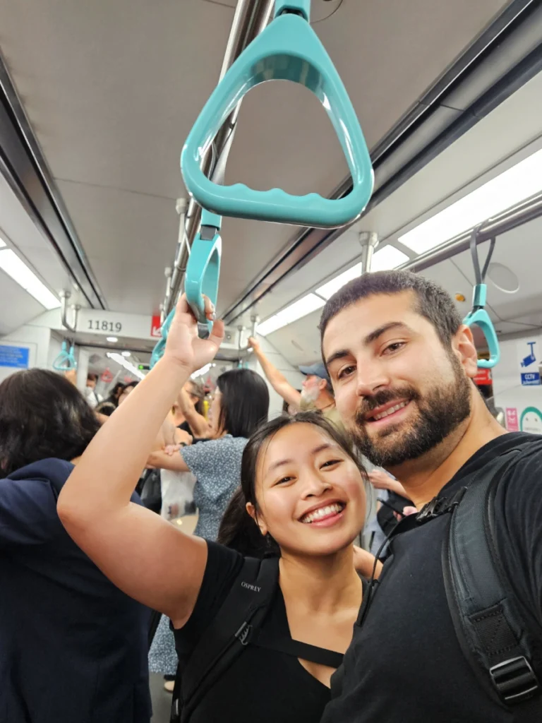 Tim and Zoe on subway in Singapore holding the dangling handles and smiling.