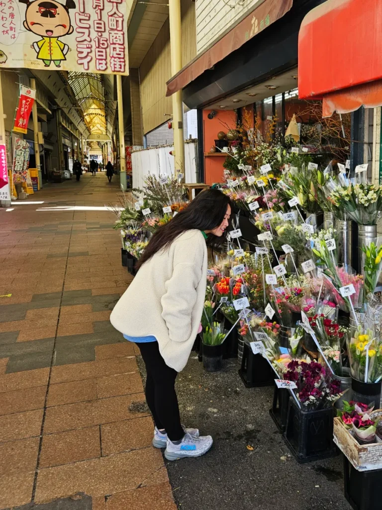 Zoe leaning over and enjoying the sight and smells of various arranged flower bouquets at a shopping arcade in Fukuoka, Japan.