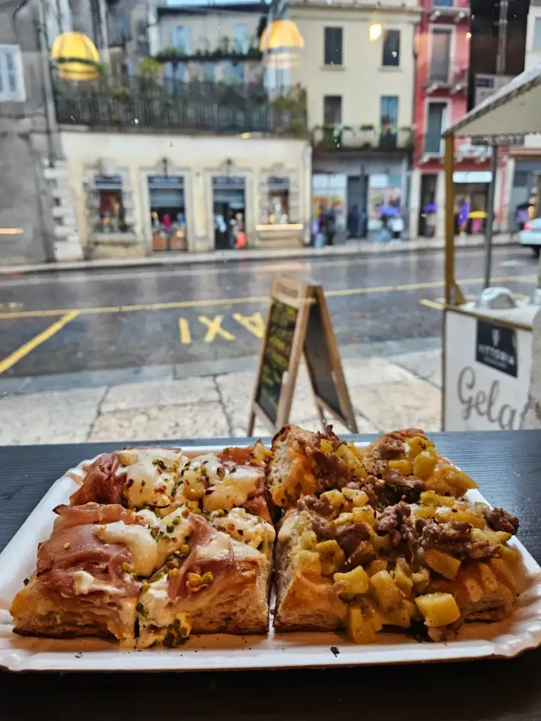 A yummy looking focaccia pizza on a counter with a window view of a street in Verona.