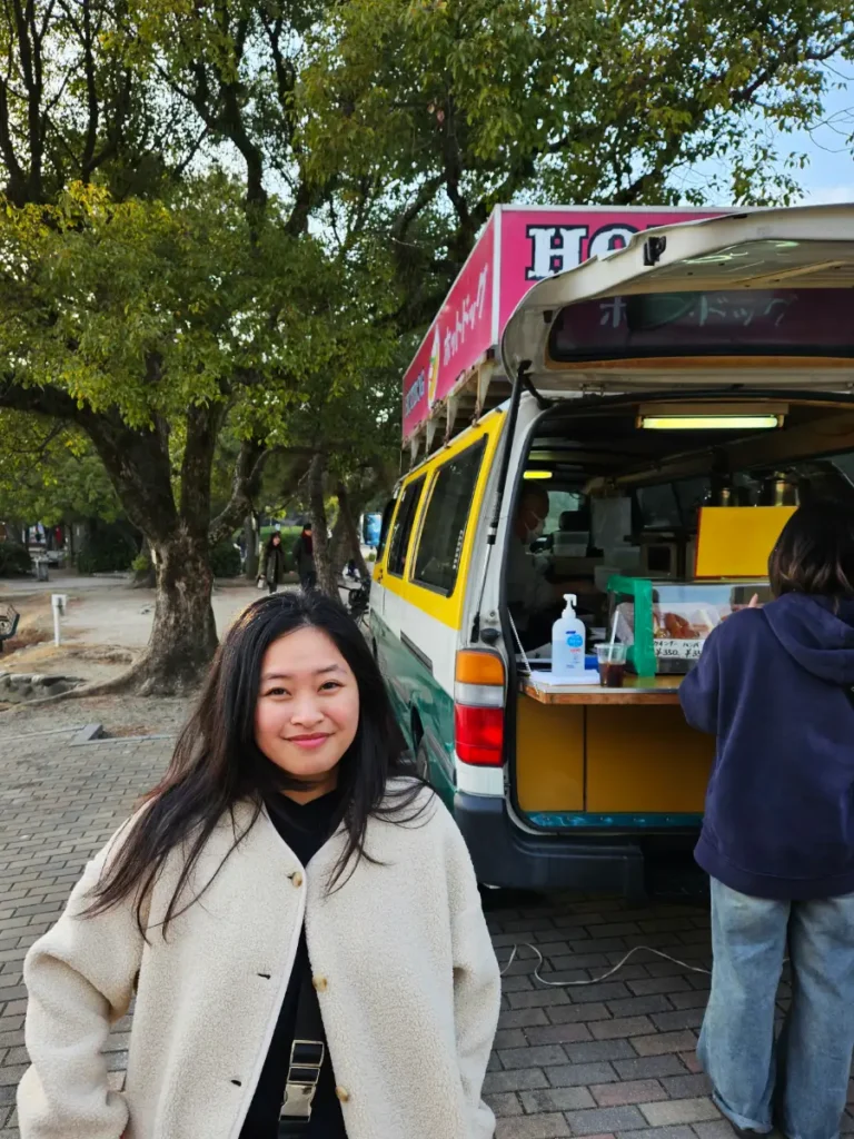 Zoe standing in front of a van selling hot dogs next to Ohori Lake.