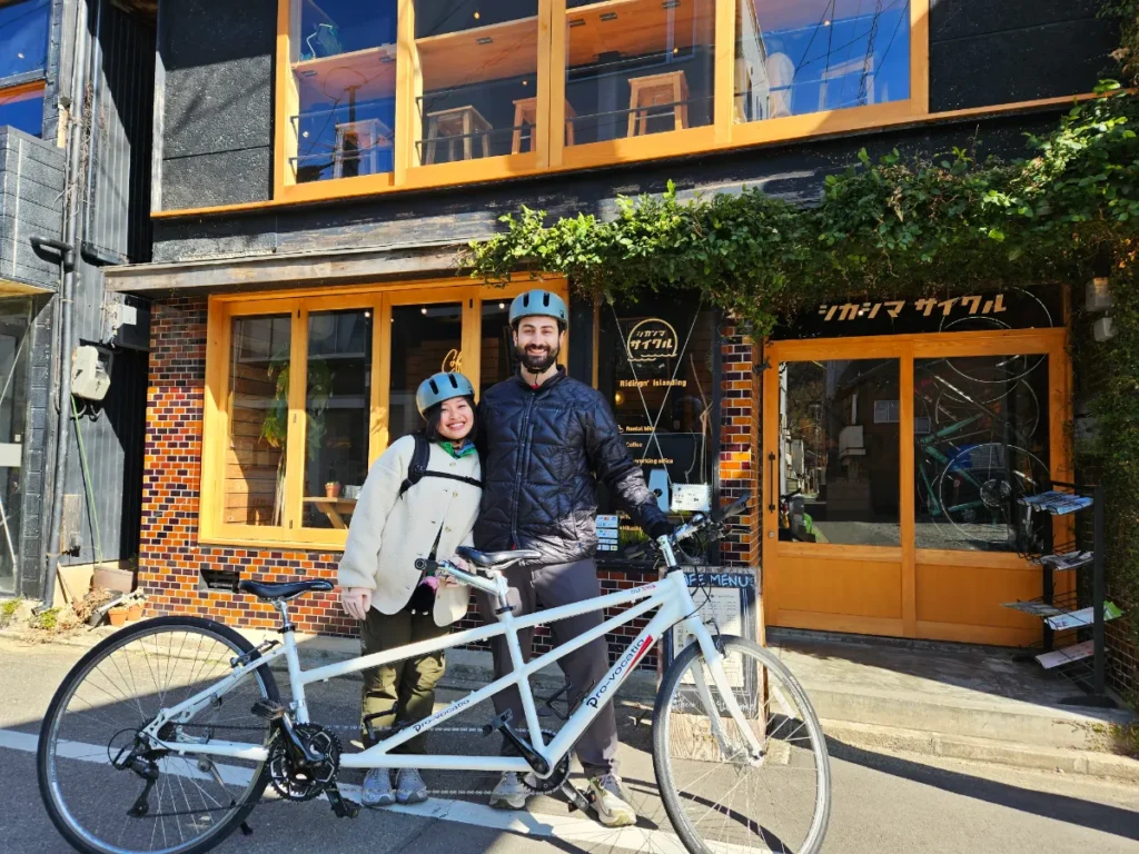 Tim and Zoe posing with their rented tandem bike in front of Shikashima Cycle.