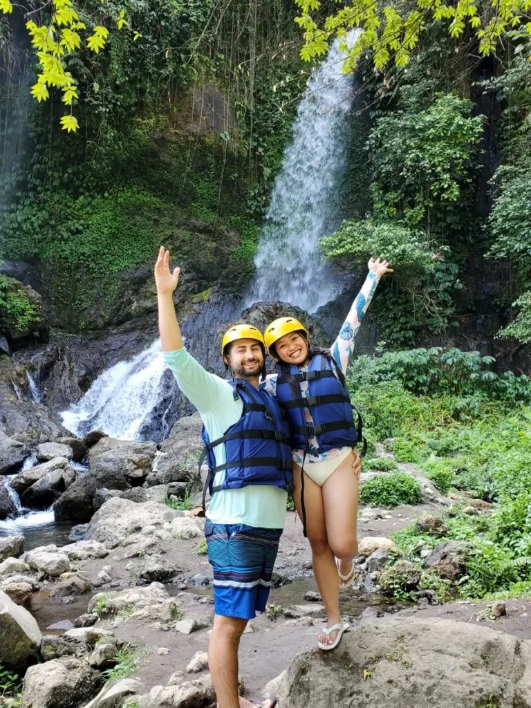 Tim and Zoe in front of a waterfall during a river rafting tour in Sideman, Bali, Indonesia. Image portrays an example of a fast travel activity during the discussion of slow travel vs. fast travel.