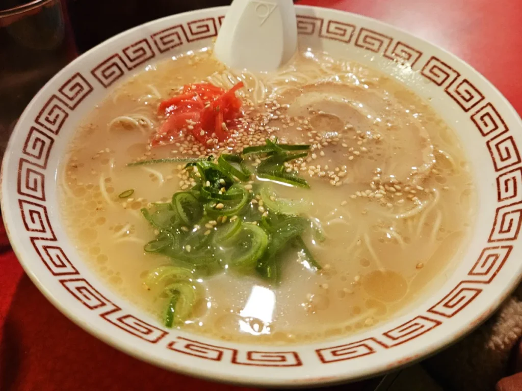 Succulent bowl of Hakata ramen with green onions, pink ginger, and sesame seeds.