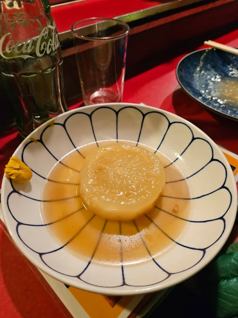 Tender radish oden sitting in broth in a white bowl with a dollop of spicy mustard on the side.