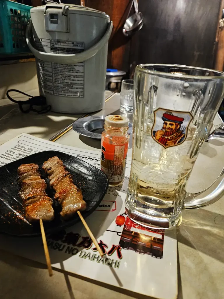 Charcoal grilled pork belly and onion yakitori accompanied by a whisky highball stein.