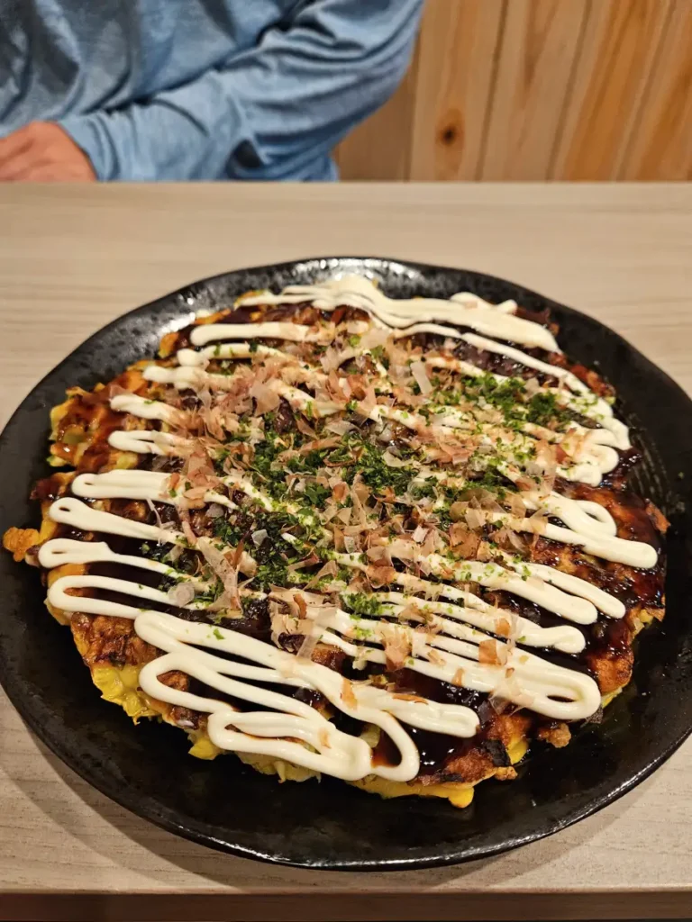 Delicious looking okonomiyaki on a black plate covered in bonito flakes and japanese mayo.