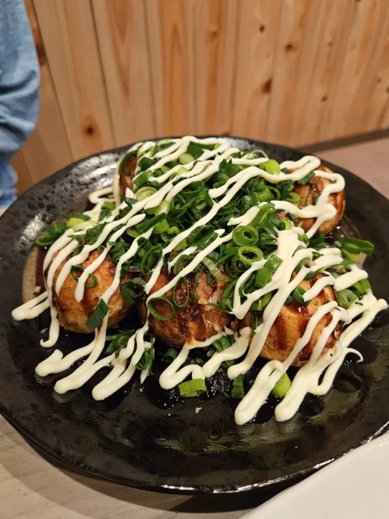 Nicely fried takoyaki on a black plate topped with green onions and japanese mayo.