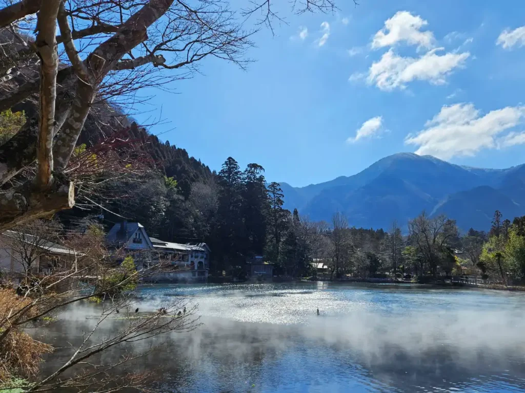 A serene view of Lake Kinrin with mist rising from the water’s surface and mountains in the distance.