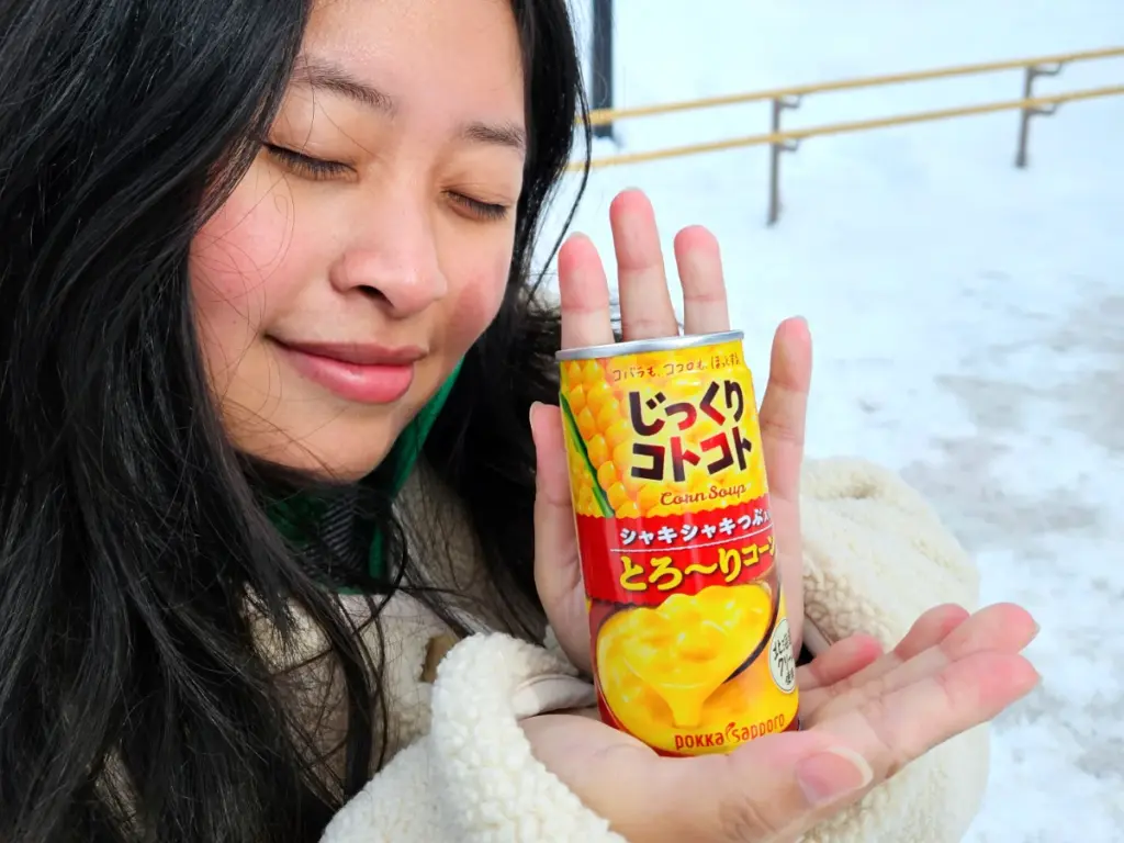 Zoe using a hot can of vending machine corn soup to warm her hands from the freezing temperatures during a winter in Hokkaido.