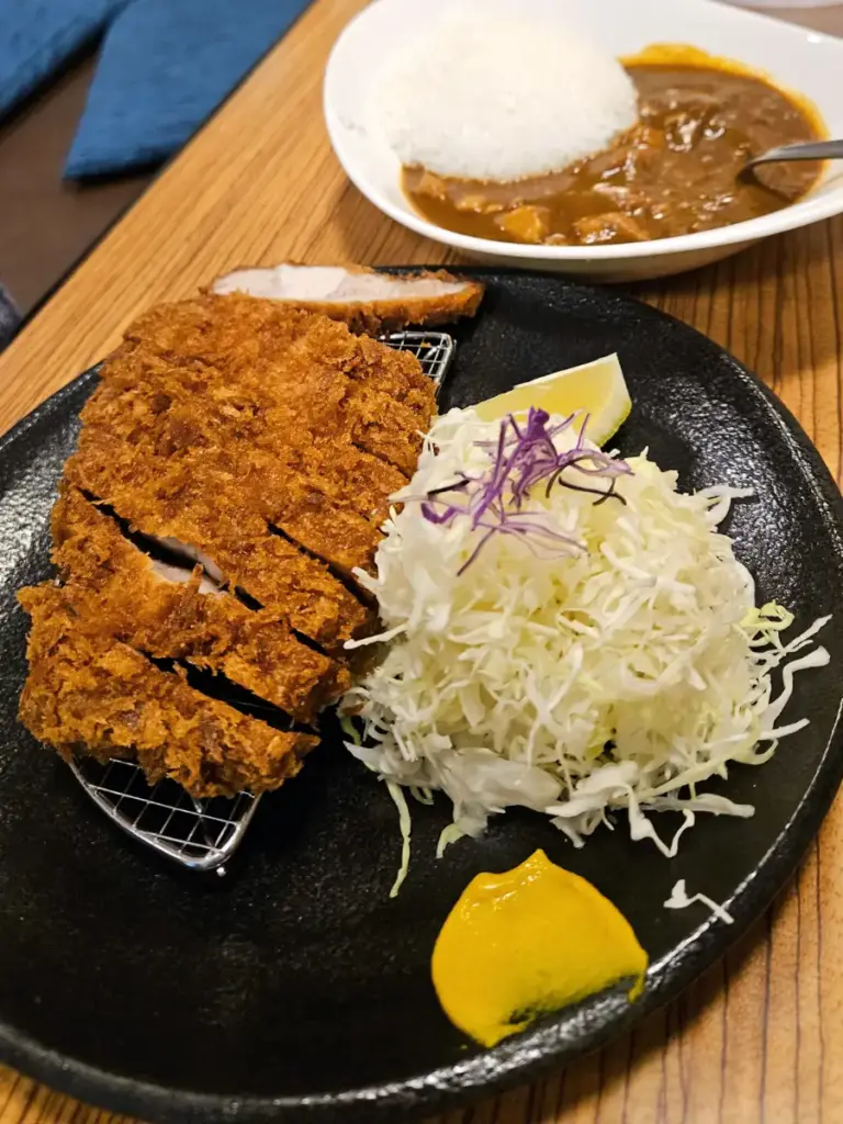 A plate of thick, golden-fried pork katsu with shredded cabbage, served alongside a bowl of rich curry and rice from Tonkatsu Kyohei in Sapporo.