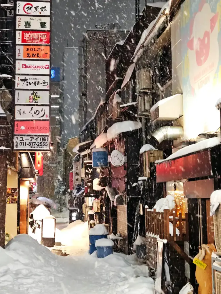 An alley with brightly lit shops covered in snow in Sapporo.