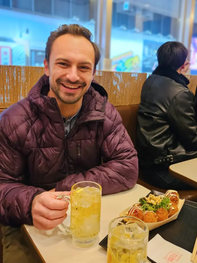 A smiling sage enjoying takoyaki and whiskey highballs in Sapporo.