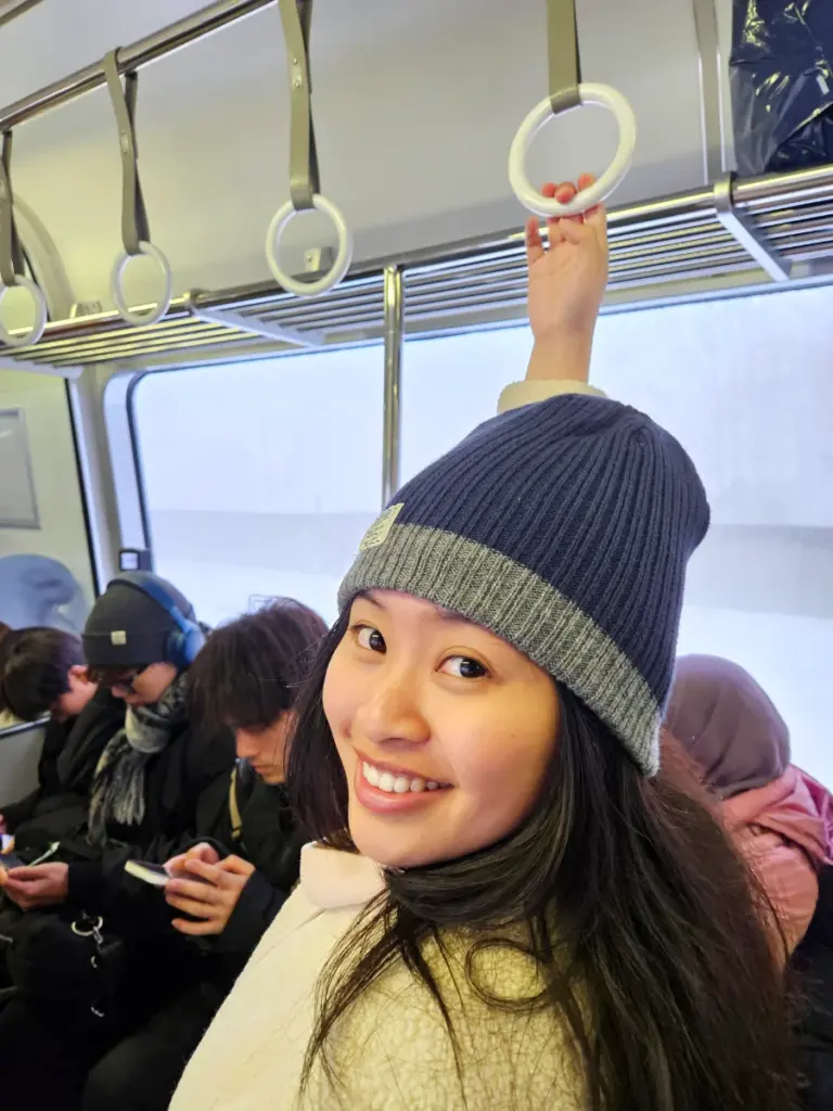 Zoe smiling and holding onto a hand ring while riding a crowded train on the long journey to Niseko during our winter in Hokkaido.