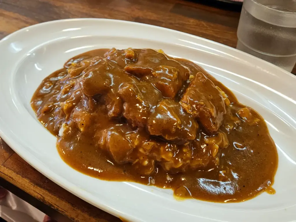 A large portion of crispy pork katsu covered in thick, rich brown curry sauce over rice from Hinoya Curry in Tokyo.