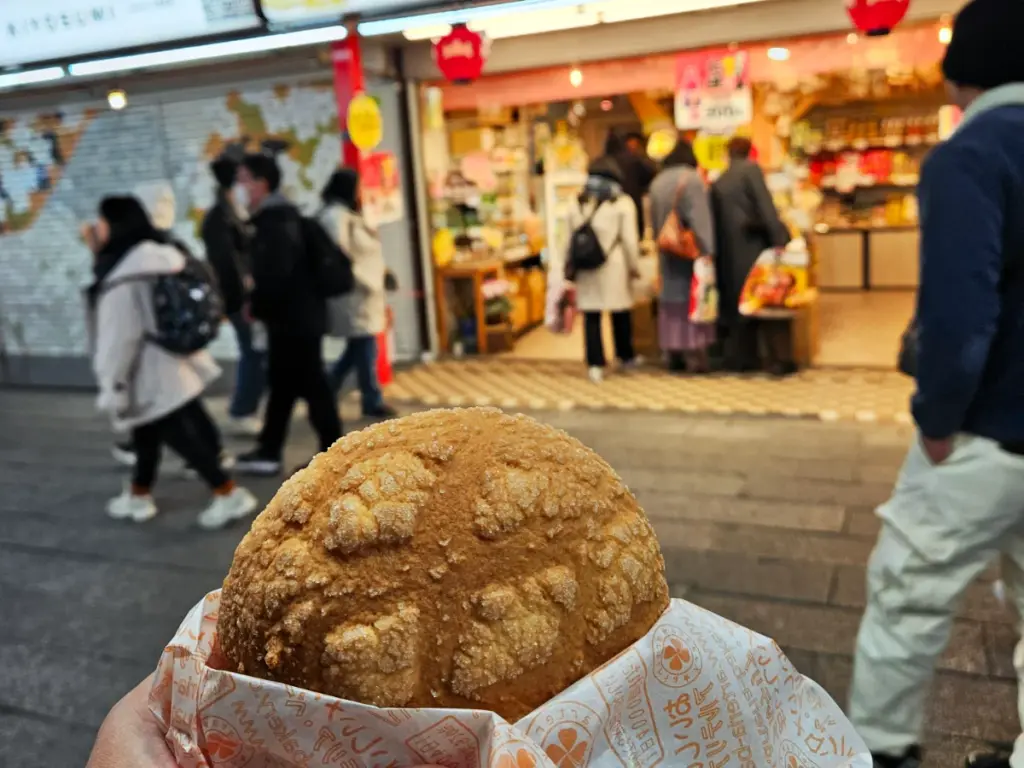 A close-up of a melonpan bun with a bustling Tokyo street in the background.