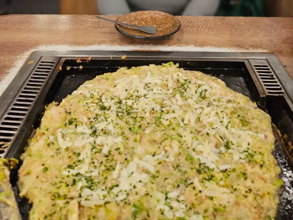 Savory, gooey monjayaki batter mixed with ingredients sizzling and cooking on a hot flat top grill at a local restaurant in Tokyo.