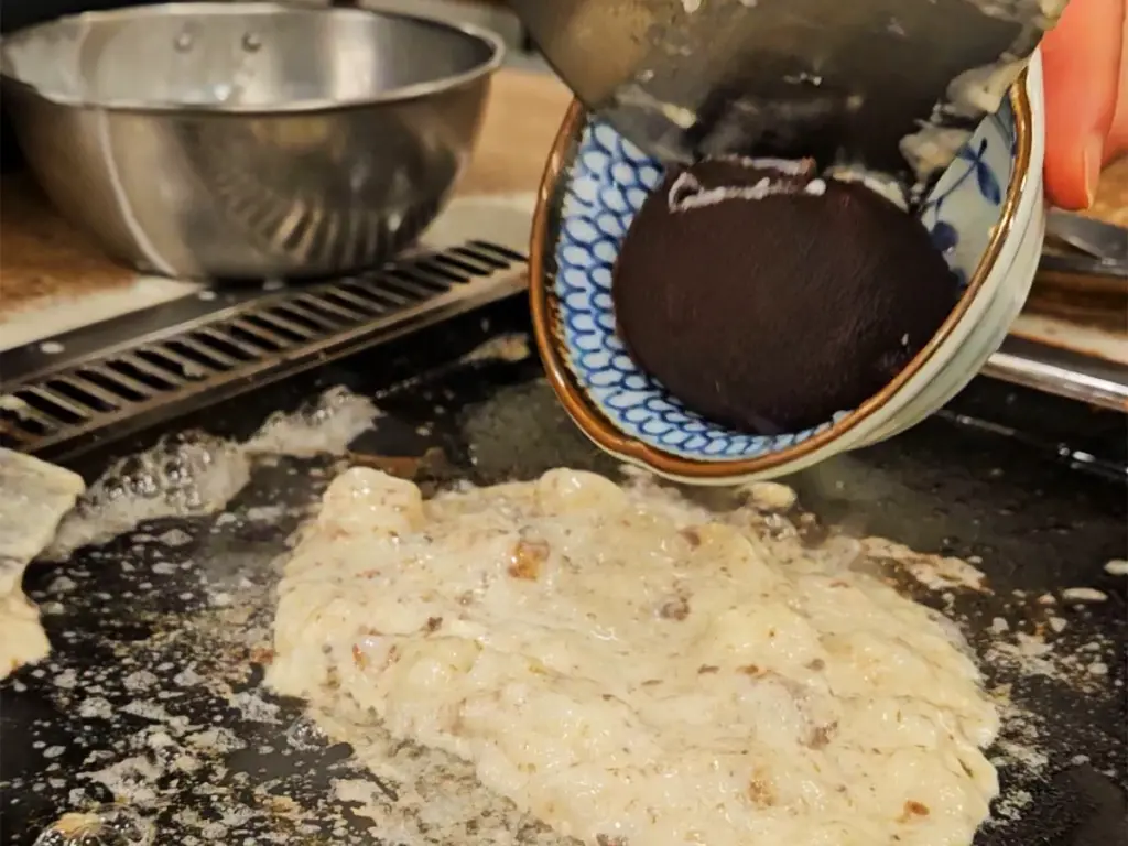 A large ball of dark, sweet red bean paste scooped onto a hot teppanyaki grill to cook a red bean mochi monjayaki dessert.