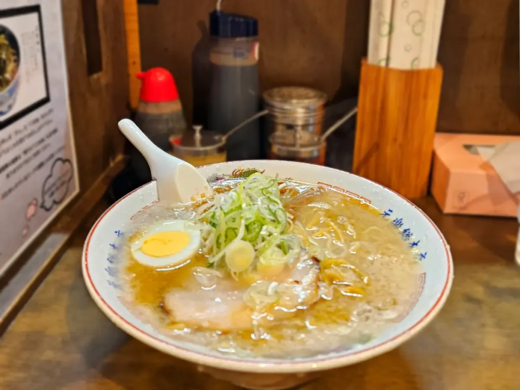 A bowl of rich seabura ramen at Genraku in Tokyo, with pork back fat broth, chashu pork, sliced green onions, and half of a boiled egg.