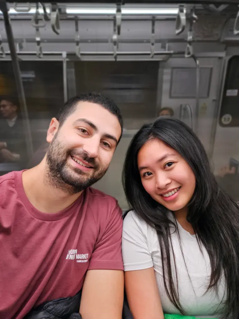 Zoe and Tim smiling together while riding inside a clean, uncrowded Tokyo commuter train.