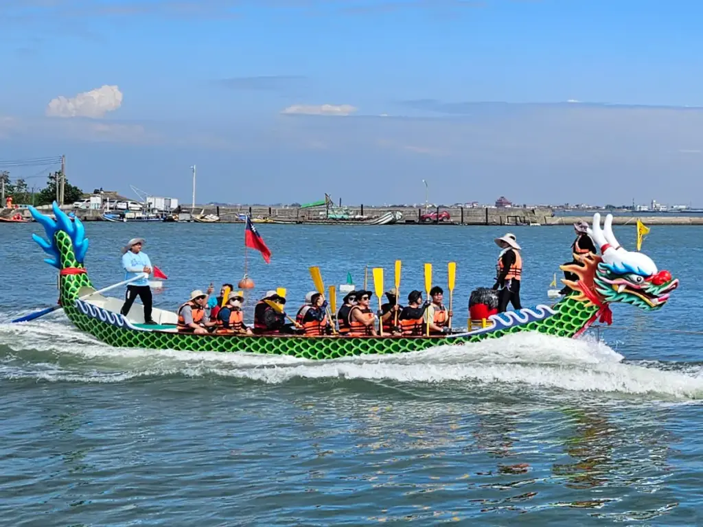 A brightly painted green dragon boat filled with a team of rowers navigating the harbor water during the Duanwu Festival.