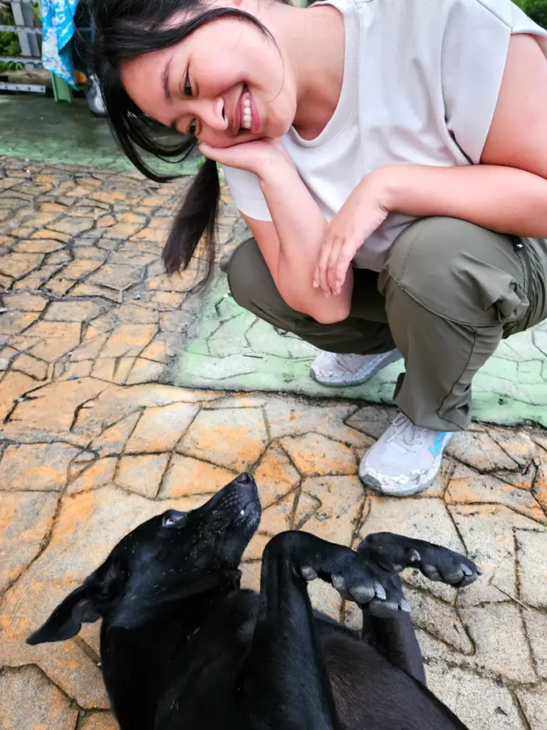 Zoe crouching down and smiling at a friendly black dog rolling on its back at the Chiayi fruit farm.