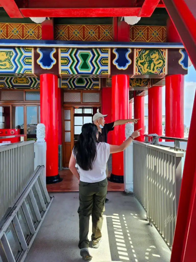 Steve pointing out into the distance while giving Zoe a tour from the balcony of a beautiful red and gold temple in Chiayi.