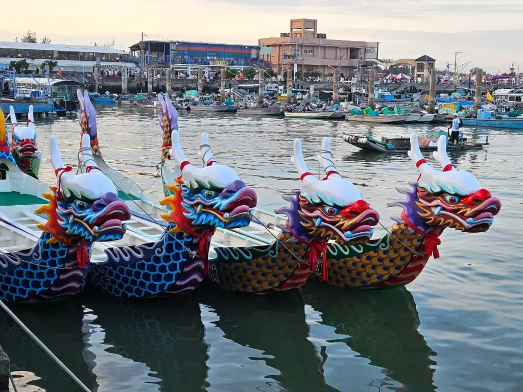 Ornate, painted dragon boats docked peacefully in the harbor water at sunset after the Dongshi Dragon Boat Festival races.