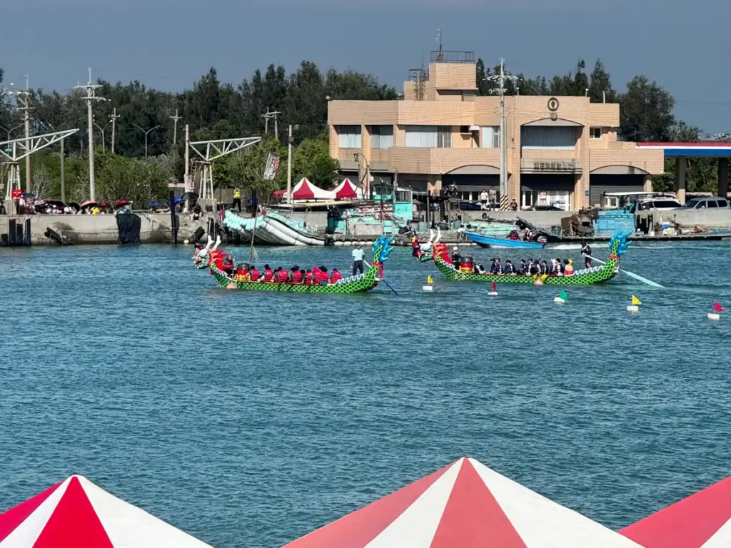 Two bright green dragon boats filled with rowers and a drummer in the water during the Duanwu Festival in Dongshi.