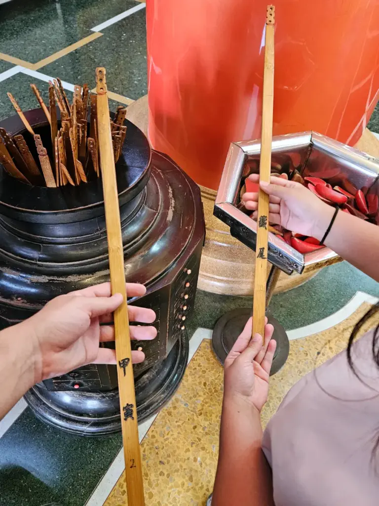 Hands holding numbered wooden kau chim fortune sticks drawn from a dark urn inside the Jiuhua Mountain Temple in Chiayi.