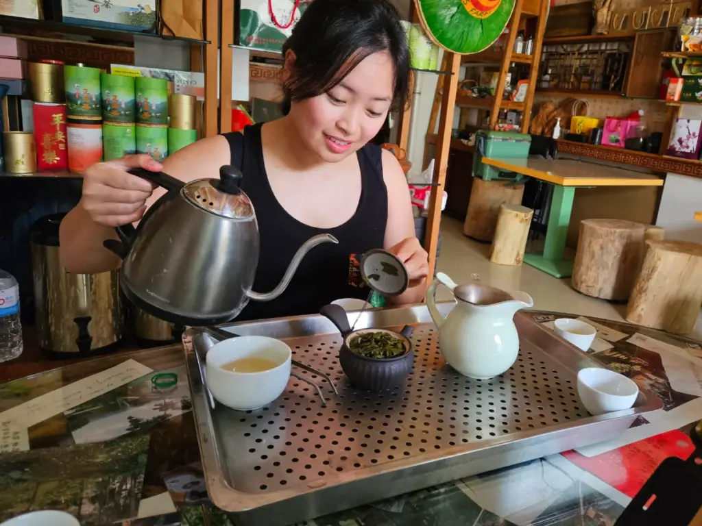 Zoe smiling while carefully pouring hot water into a teapot, learning to perform a traditional Taiwanese tea ceremony.