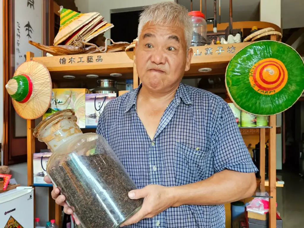 Steve, the tea shop owner, holding a massive glass jar filled with dried tea leaves, sharing his passion for Taiwanese tea culture.
