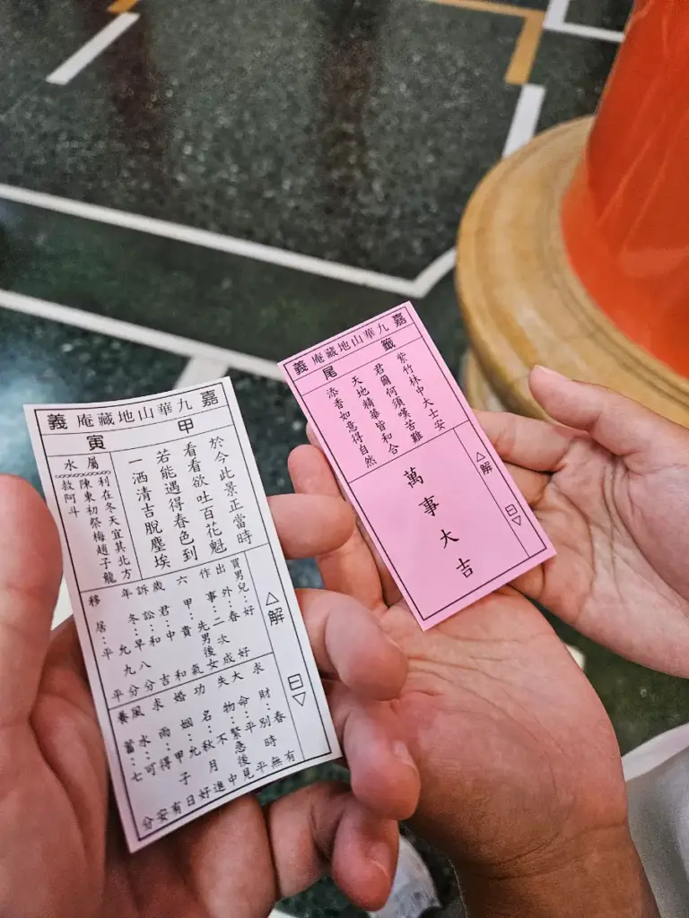 Two hands holding a rare red auspicious kau chim fortune and a white good luck fortune drawn at a local Chiayi temple.