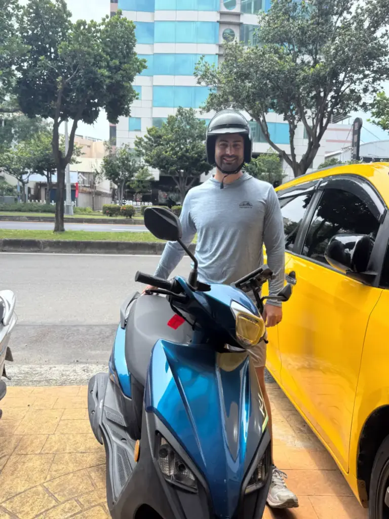 Tim standing next to a blue rental scooter in Taiwan, preparing for the ride to the Dongshi Dragon Boat Festival.