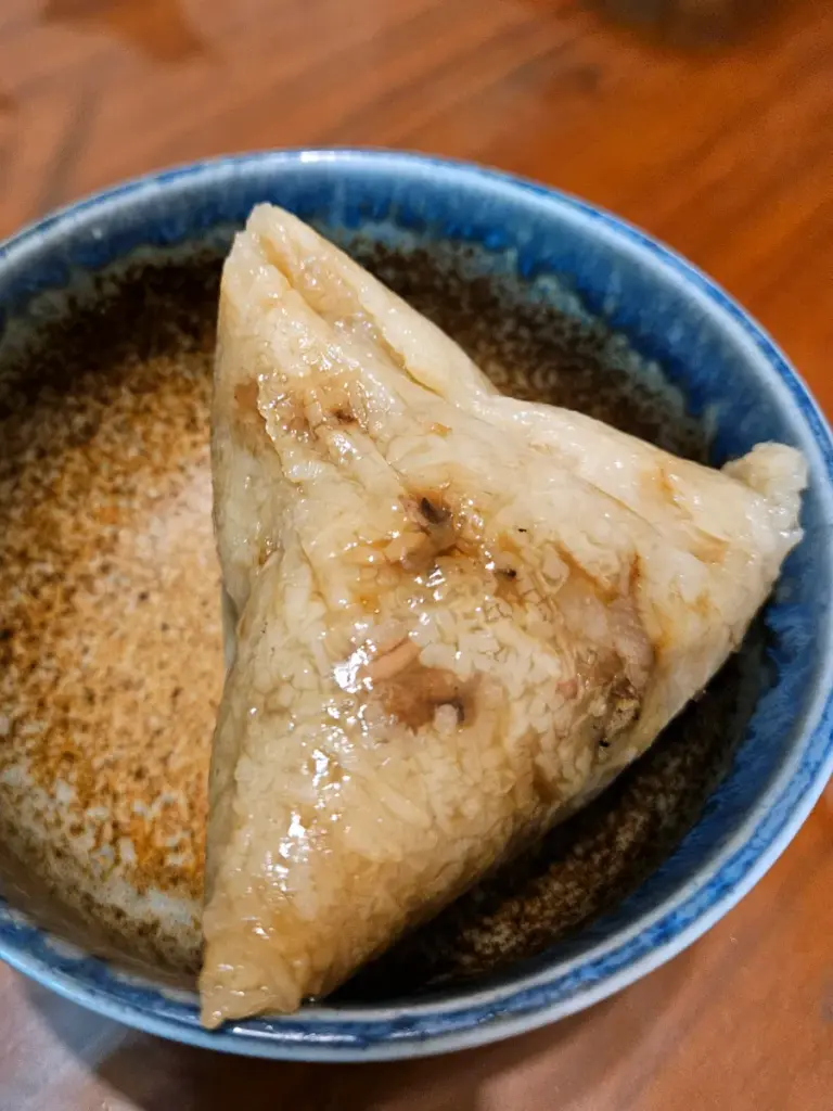 A close-up of an unwrapped, savory Taiwanese zongzi made of sticky rice sitting in a bowl.