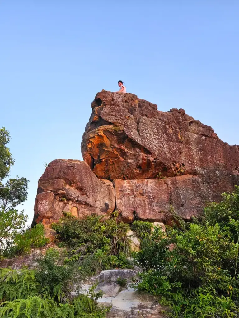 Zoe on the massive, wave-shaped sandstone crest of Battleship Rock under a clear blue sky in Taipei.