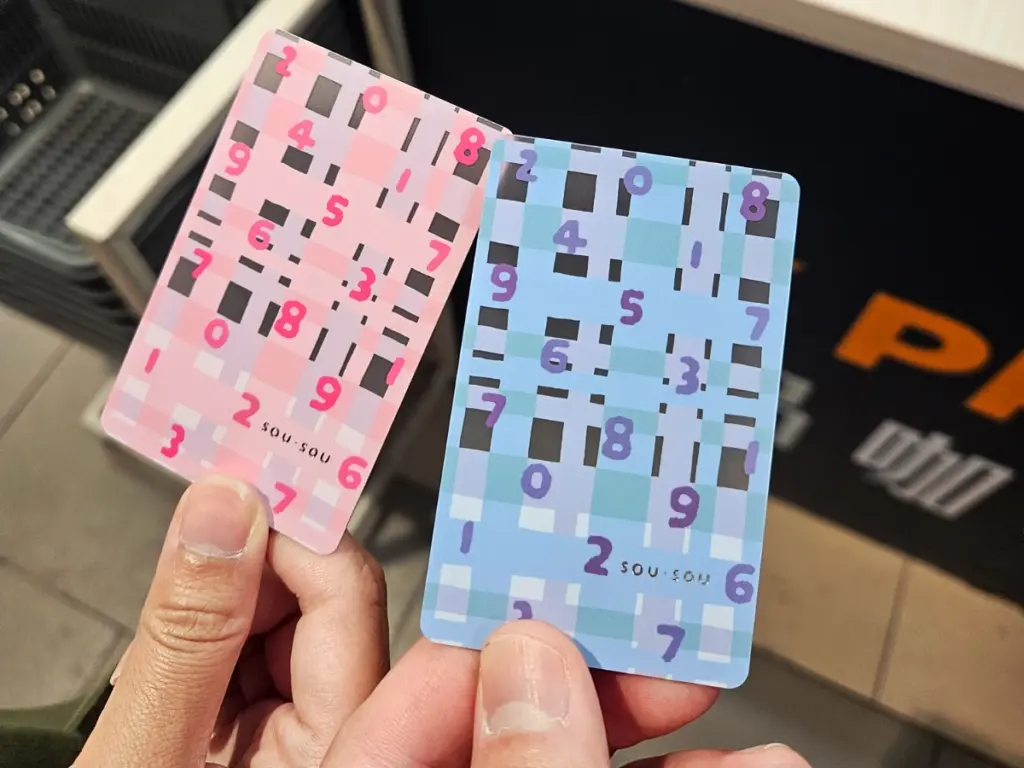 Two hands holding custom-designed pink and blue SOU・SOU patterned EasyCards used for public transportation in Taipei, Taiwan.