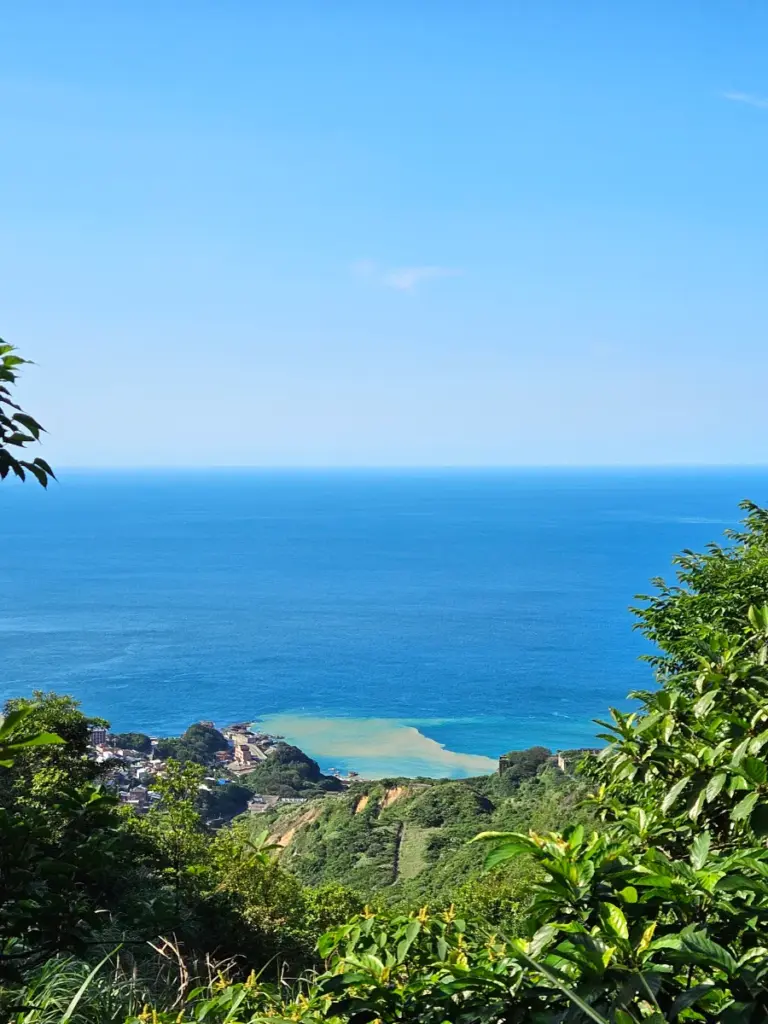 A scenic view from Teapot Mountain overlooking the Yinyang Sea, where golden mineral runoff visibly mixes with the blue ocean water.