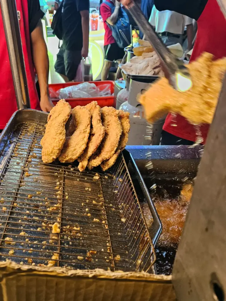 A close-up of golden-brown fried chicken cutlets being lifted out of a deep fryer with tongs.